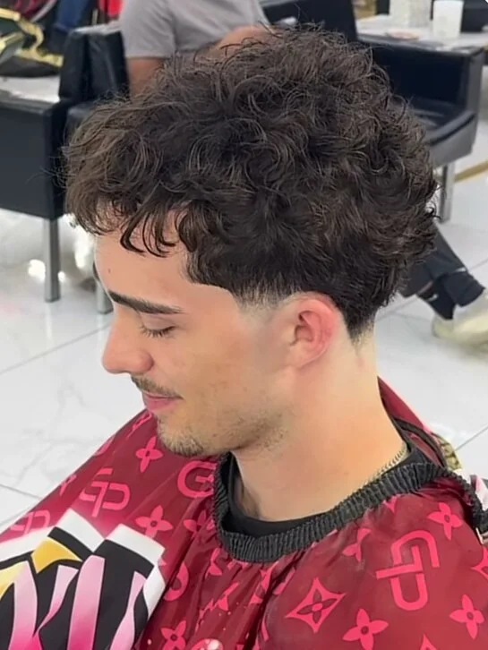 Short curly hair with a clean taper at the temple.